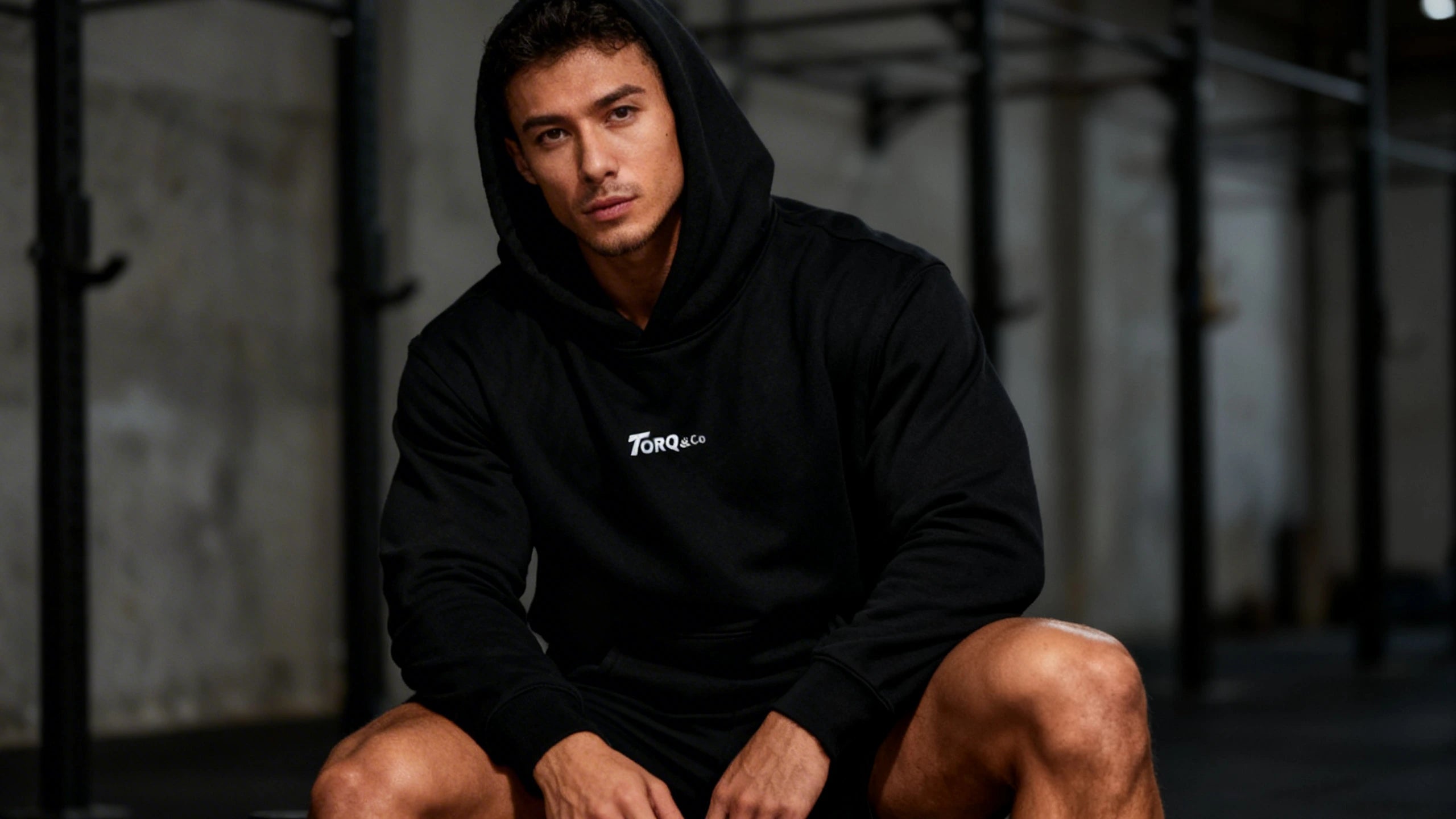 Man wearing a black Torq hoodie, sitting in a dark gym setting.